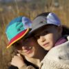 All smiles mother and daughter hiking in the fields around Johannesburg wearing trail caps in teal / jade / gold and grey / black