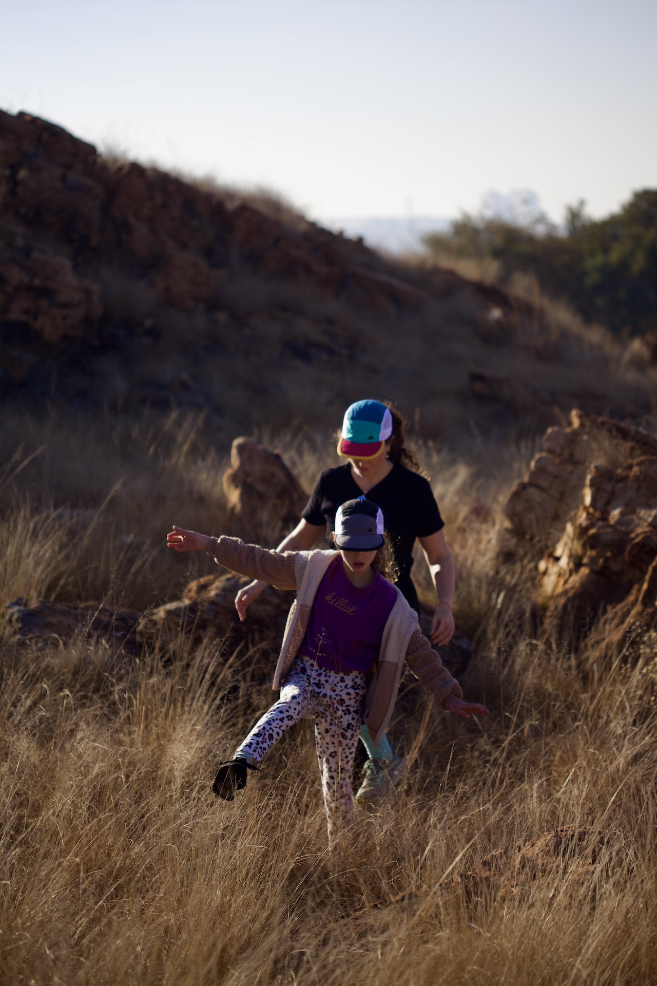 Mother and daughter hiking in the fields around Johannesburg wearing trail caps in teal / jade / gold and grey / black