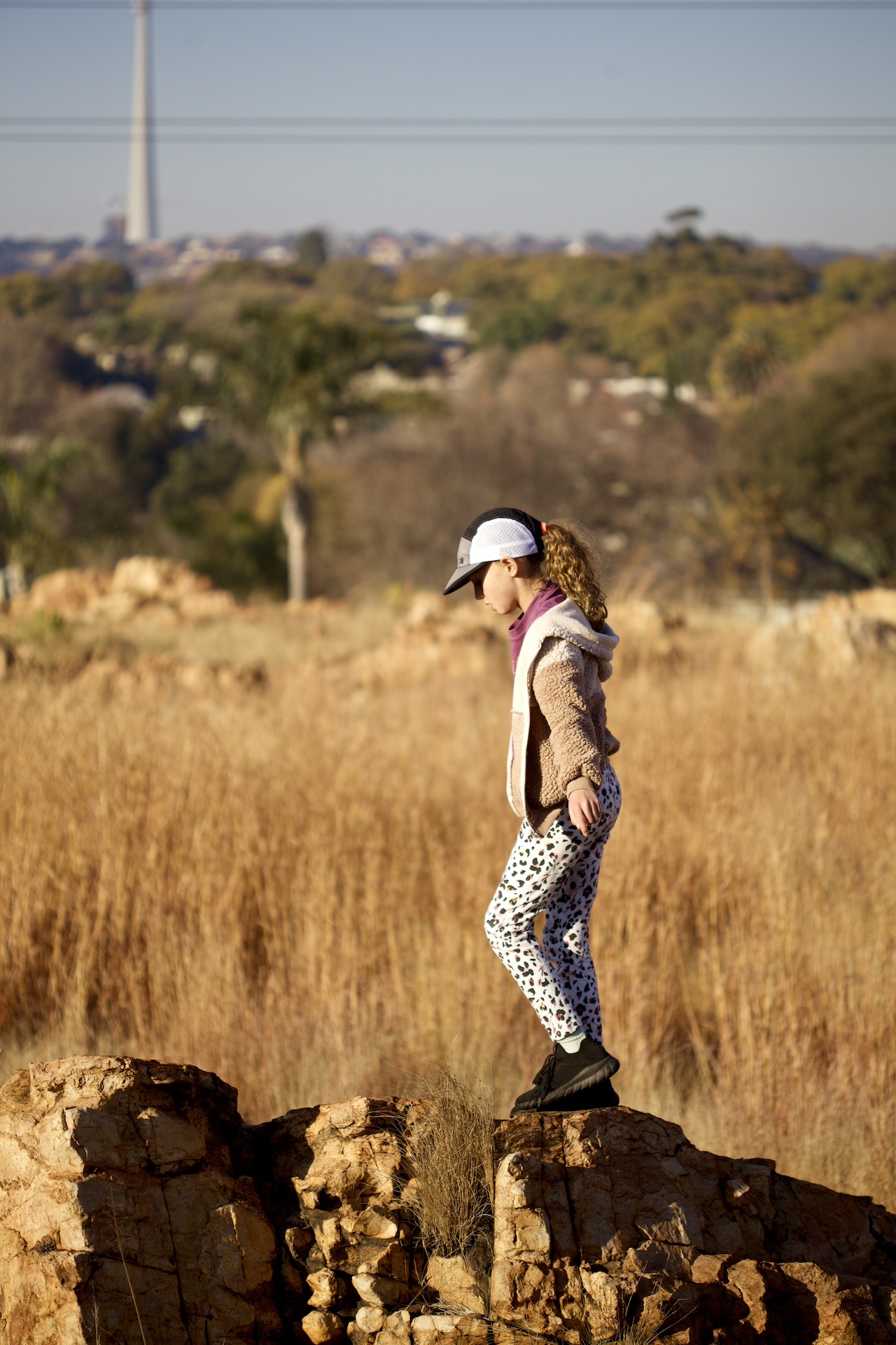 Cool kid rock hopping in the fields around Johannesburg wearing a trail caps in grey / black