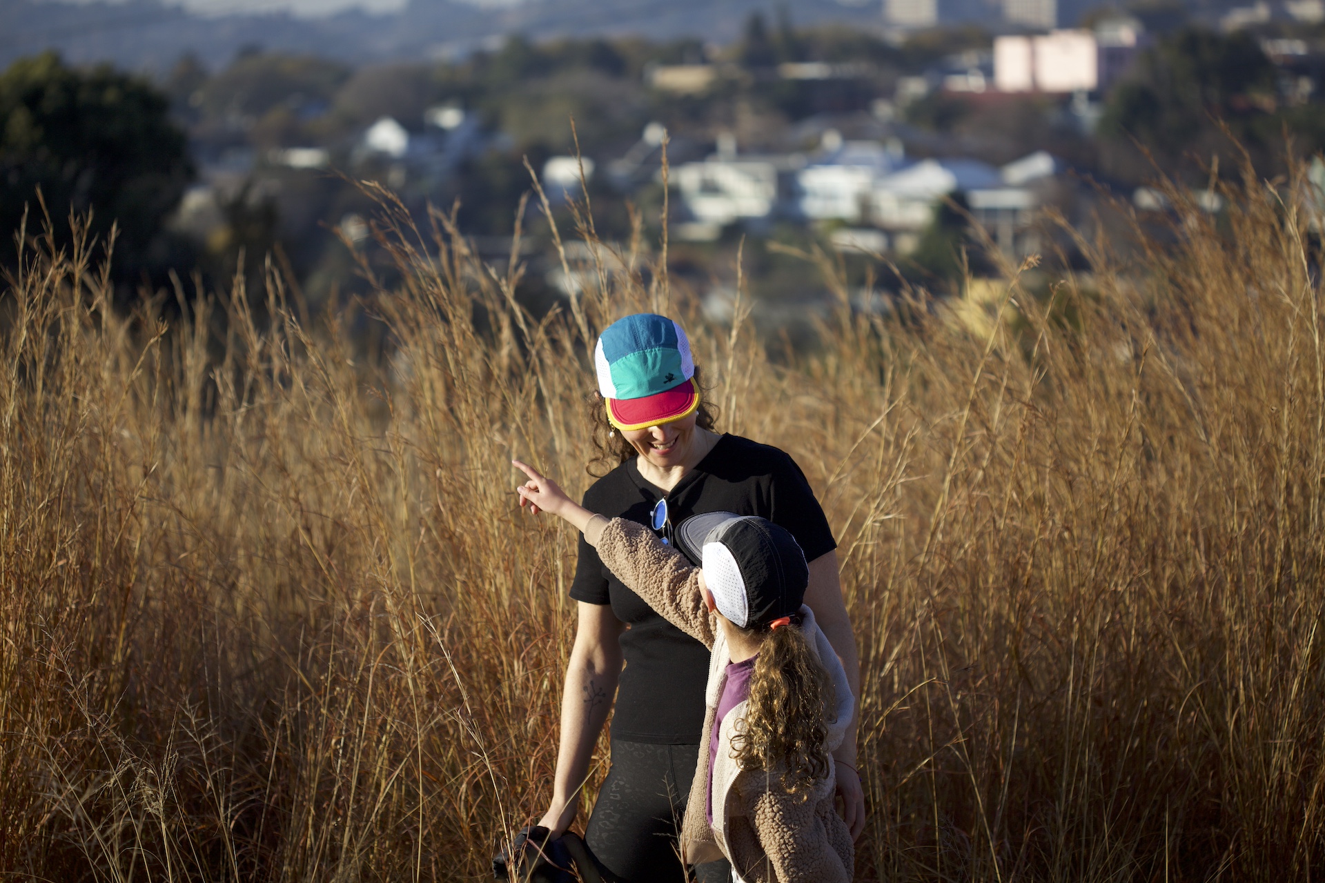 All smiles mother and daughter pointing while hiking in the fields around Johannesburg wearing trail caps in teal / jade / gold and grey / black