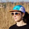Women with teal / jade / gold trail cap with a field background and wearing shades