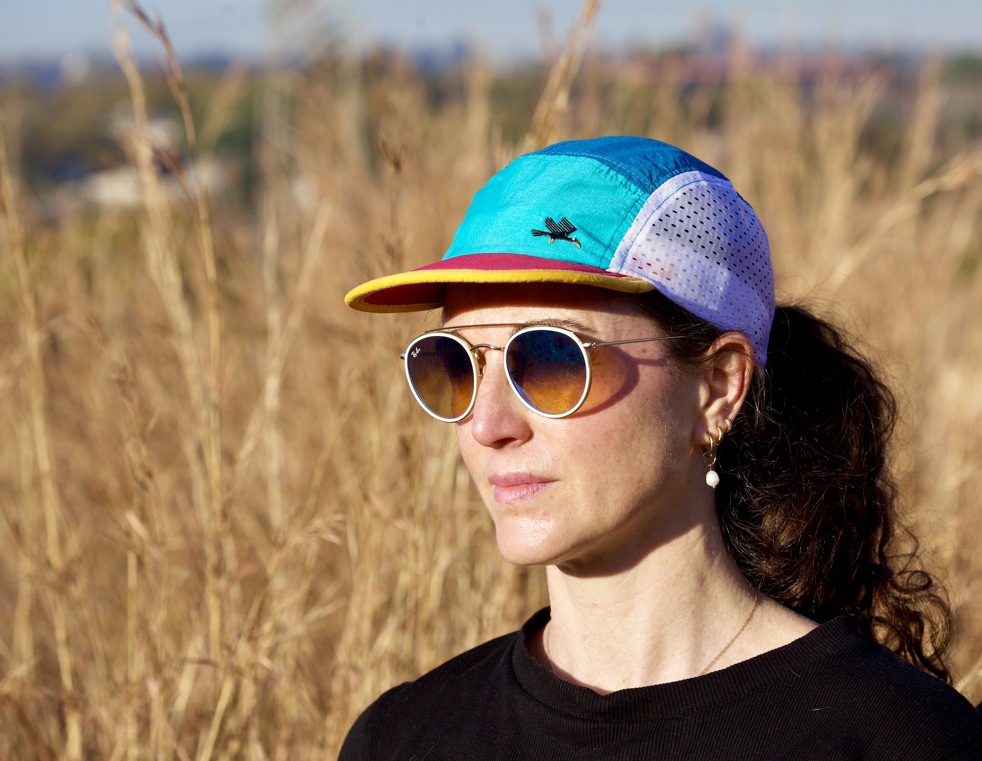 Women with teal / jade / gold trail cap with a field background and wearing shades