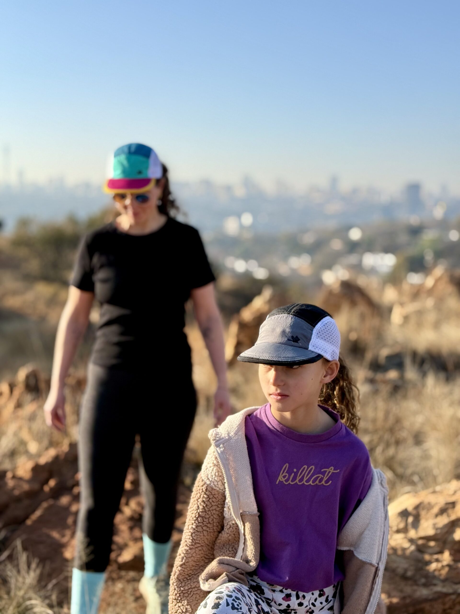 All smiles mother and daughter hiking in the fields around Johannesburg wearing trail caps in teal / jade / gold and grey / black